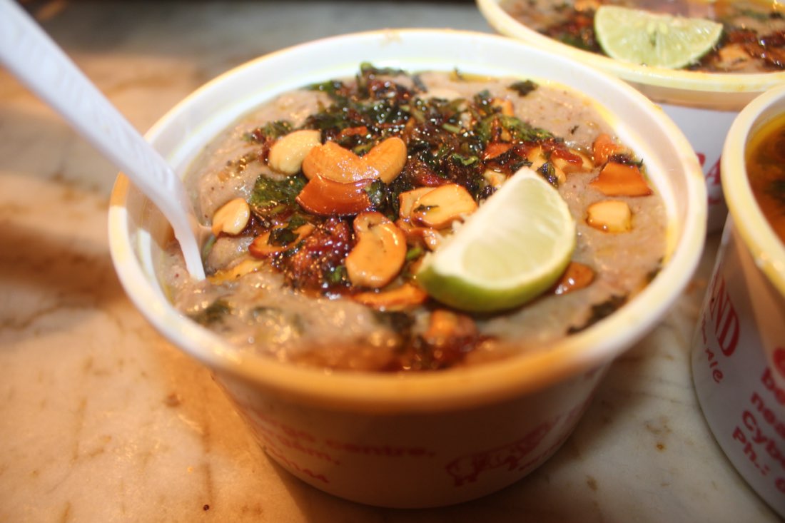 A bowl of Hyderabadi haleem garnished with fried onions, cashews and lime